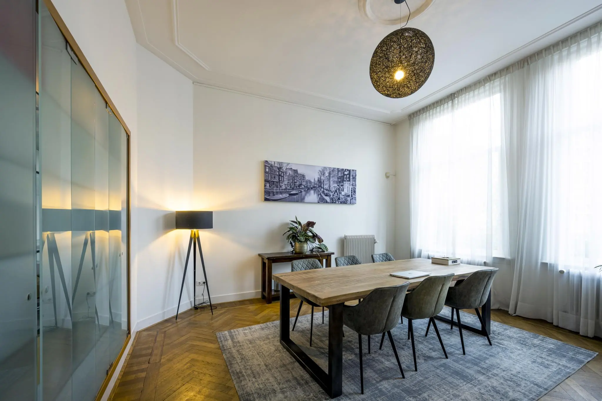 Modern ingerichte vergaderruimte aan de Van Eedenstraat met een houten tafel, zes stoelen, grote ramen en een zwart-wit foto van een Amsterdamse gracht aan de muur.